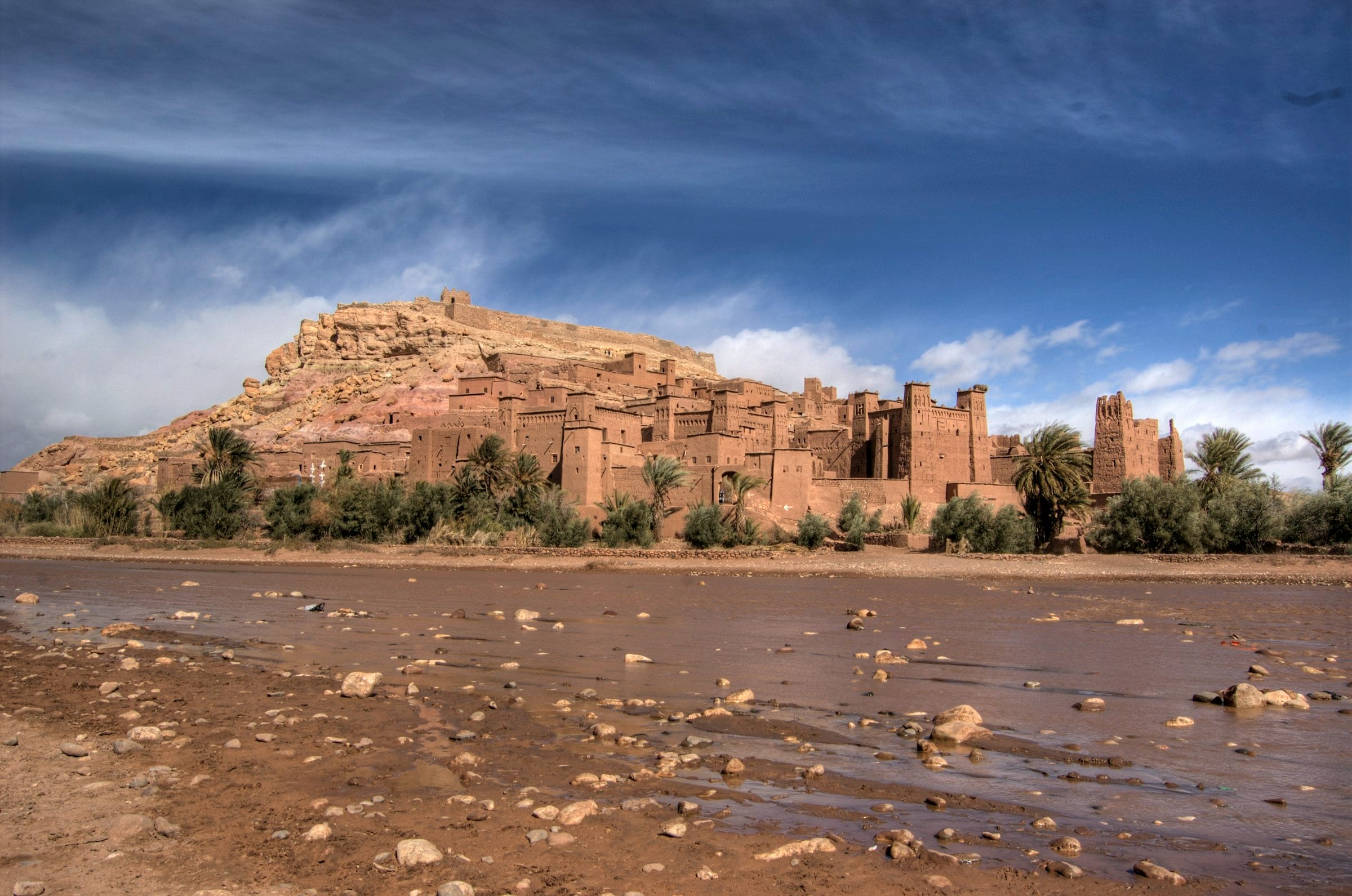Ksar de terre au bord de l'oued, vallée aride en arrière-plan
