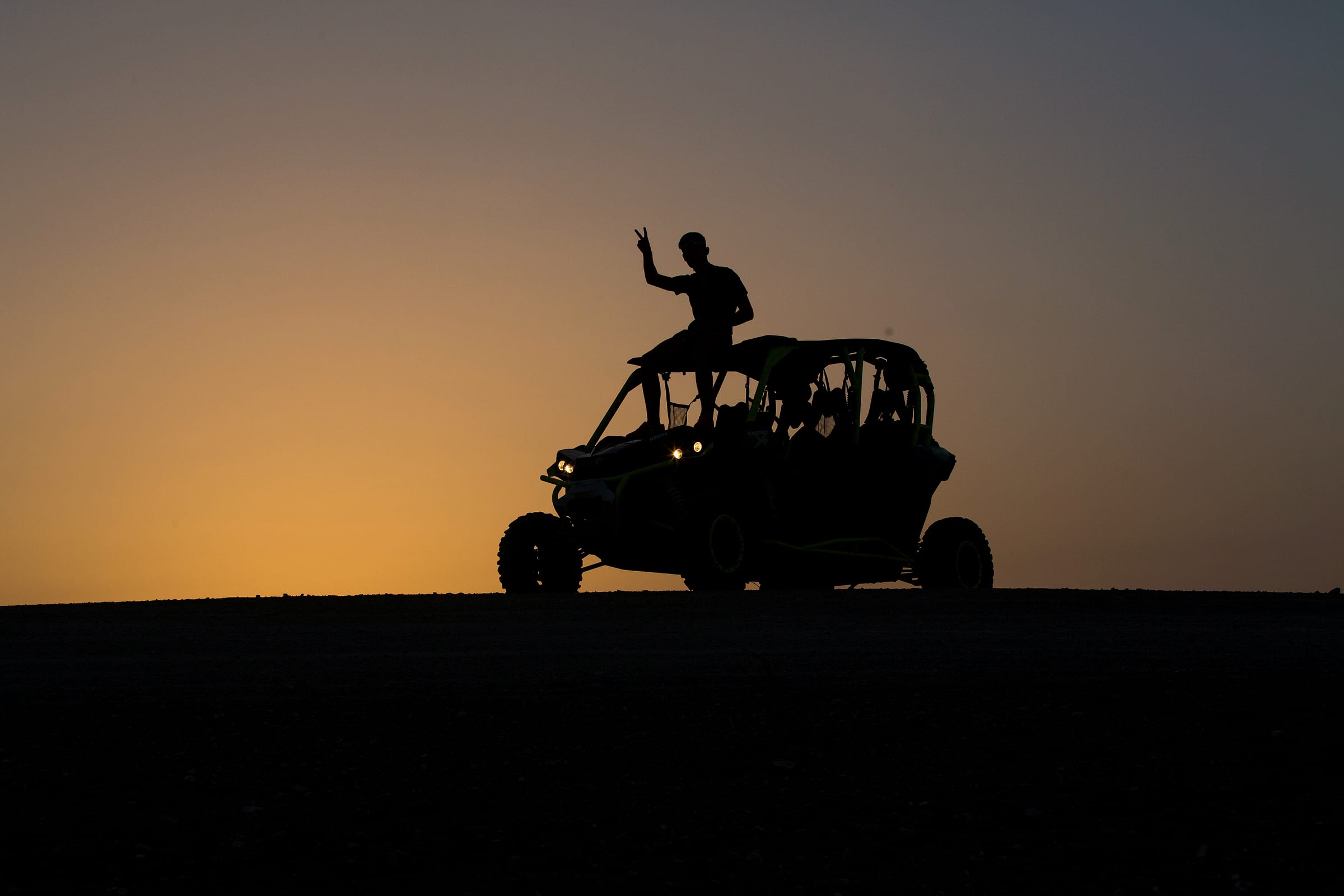 Silhouettes de pilotes bras levés sur leur buggy devant le ciel orangé du soir