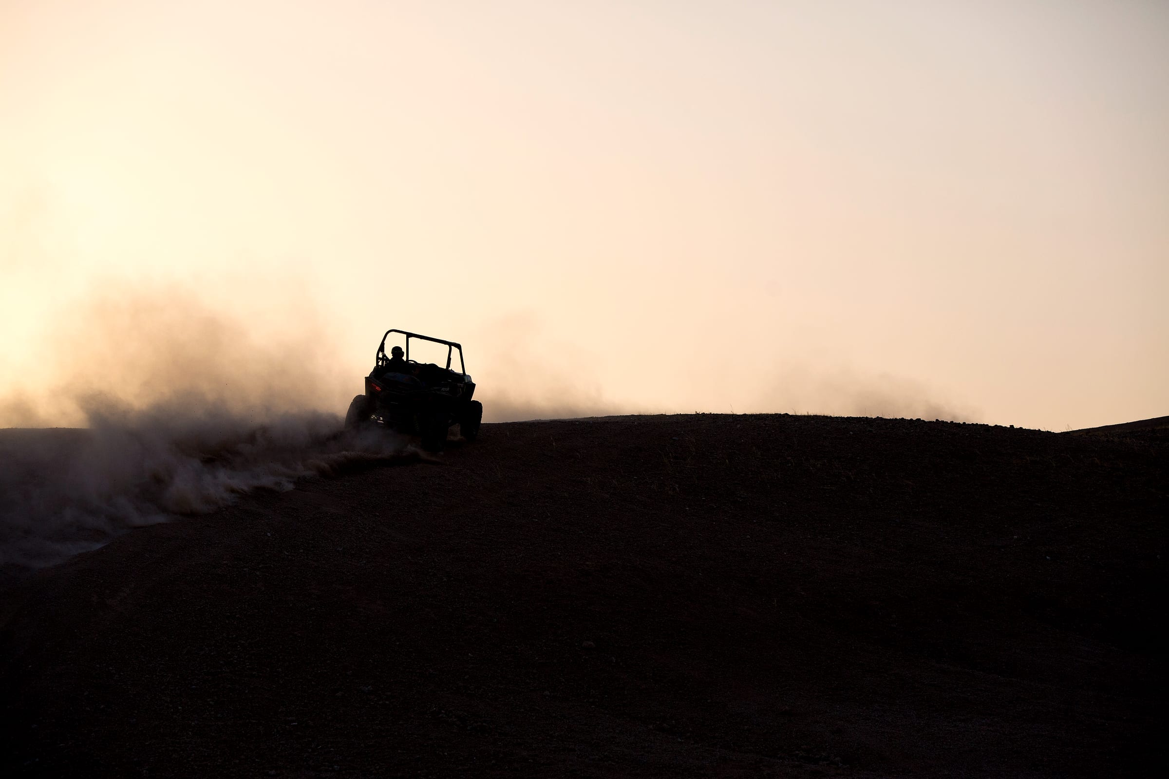 Buggy soulevant un panache de poussière en franchissant une crête rocheuse